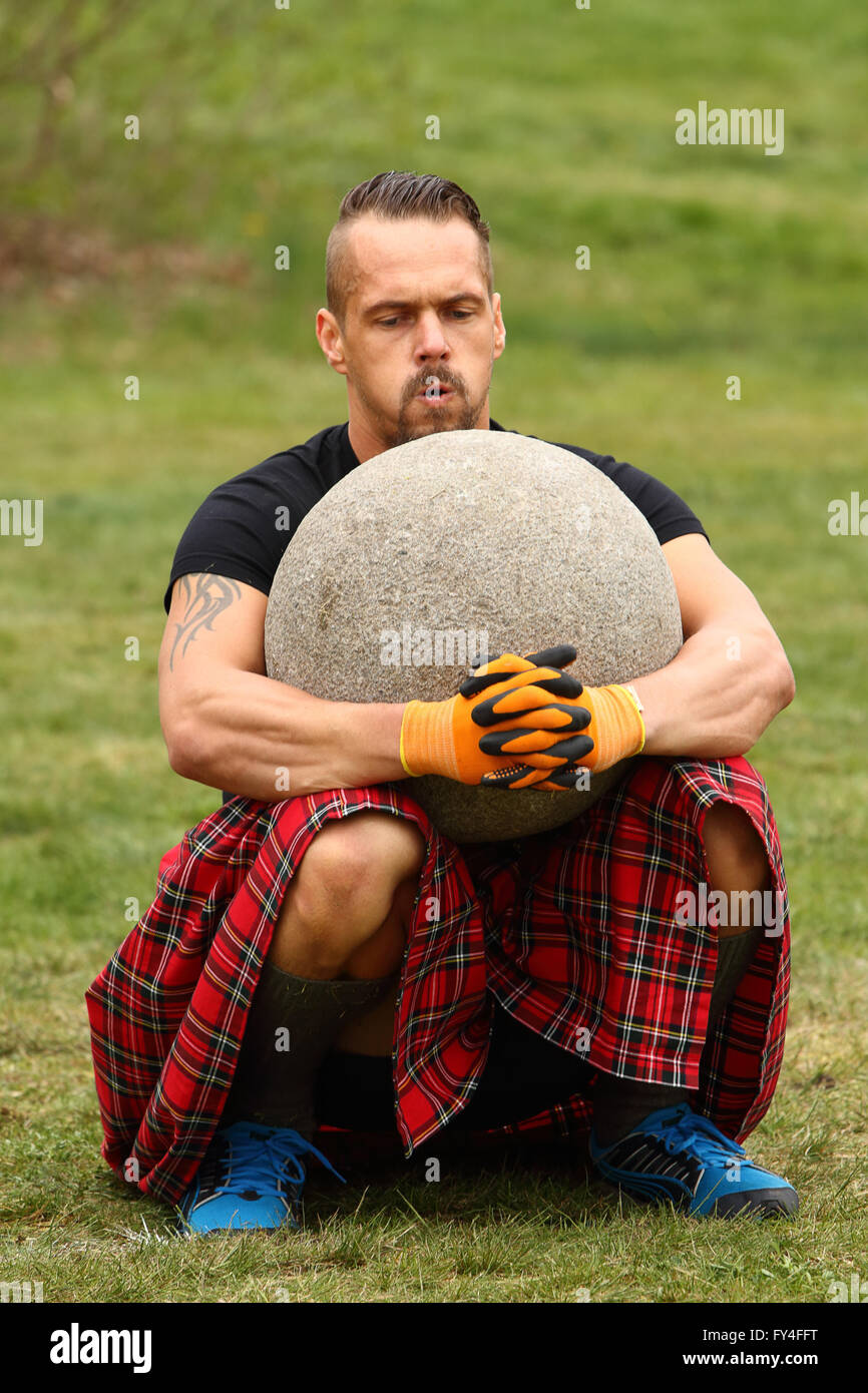 Concurrent masculin assis sur croupes avec 90 kg de poids en pierre sur ses genoux Banque D'Images