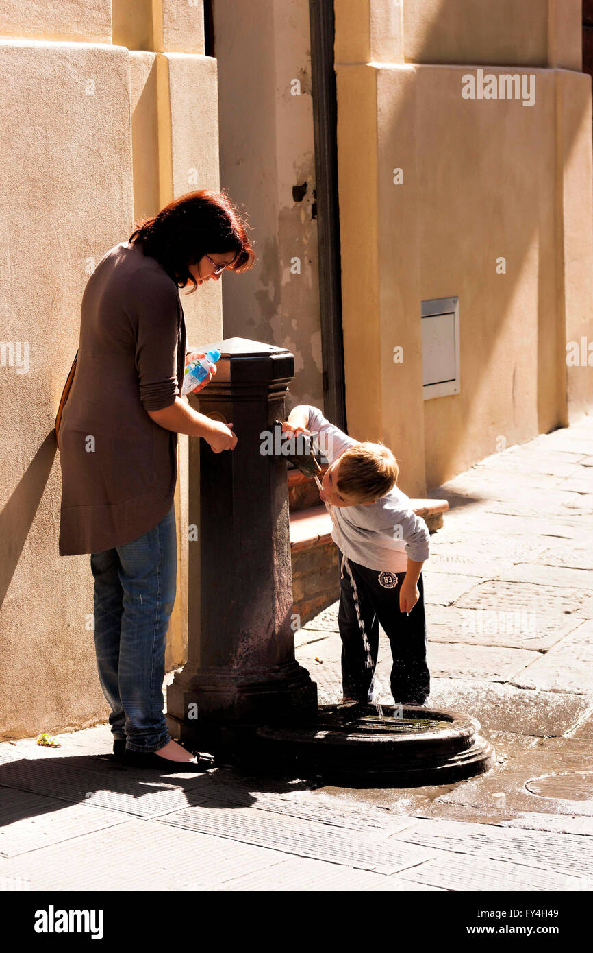 Garçon regardé par mère boire d'une fontaine d'eau rue, Sienne, Toscane, Italie Banque D'Images