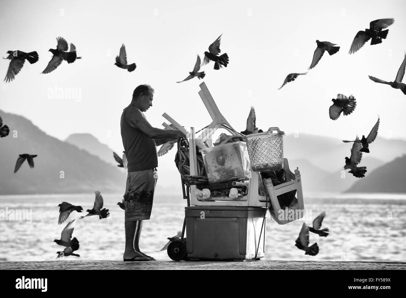 RIO DE JANEIRO - le 3 avril 2016 : une plage de Copacabana vendeur organise ses affaires comme un troupeau de pigeons passent dans le soleil du matin. Banque D'Images