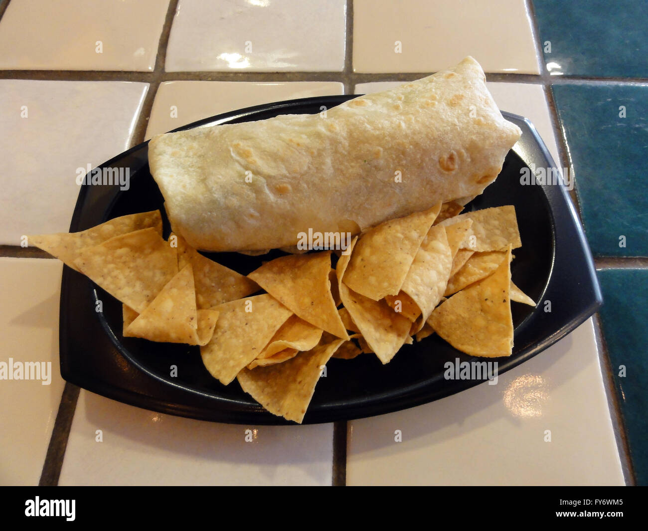 Burrito et jetons sur une plaque en plastique sur une table carrelée. Banque D'Images