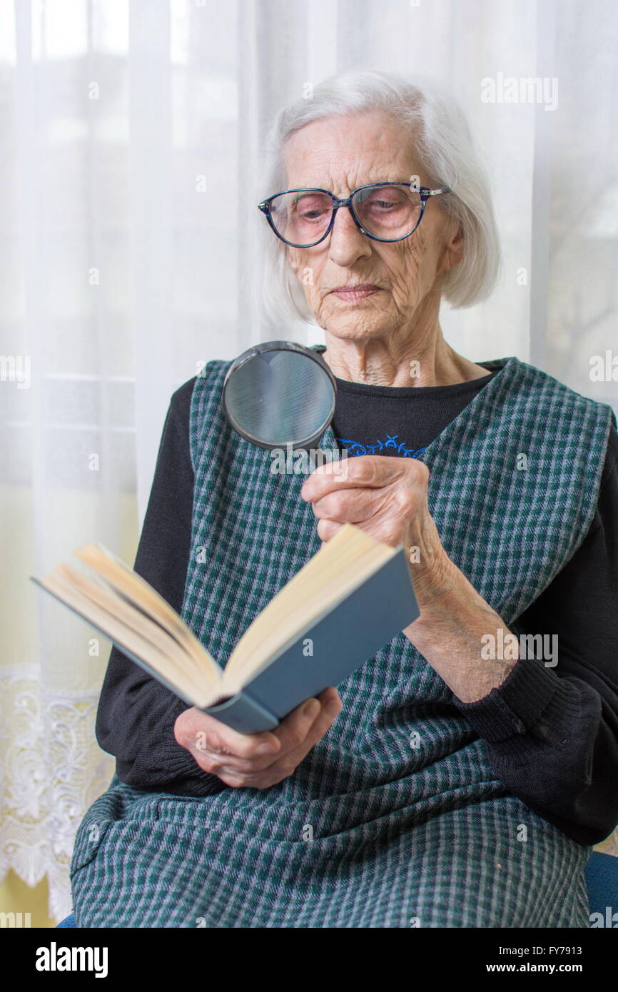 Quatre-vingt-dix ans grand-mère la lecture d'un livre par loupe Banque D'Images
