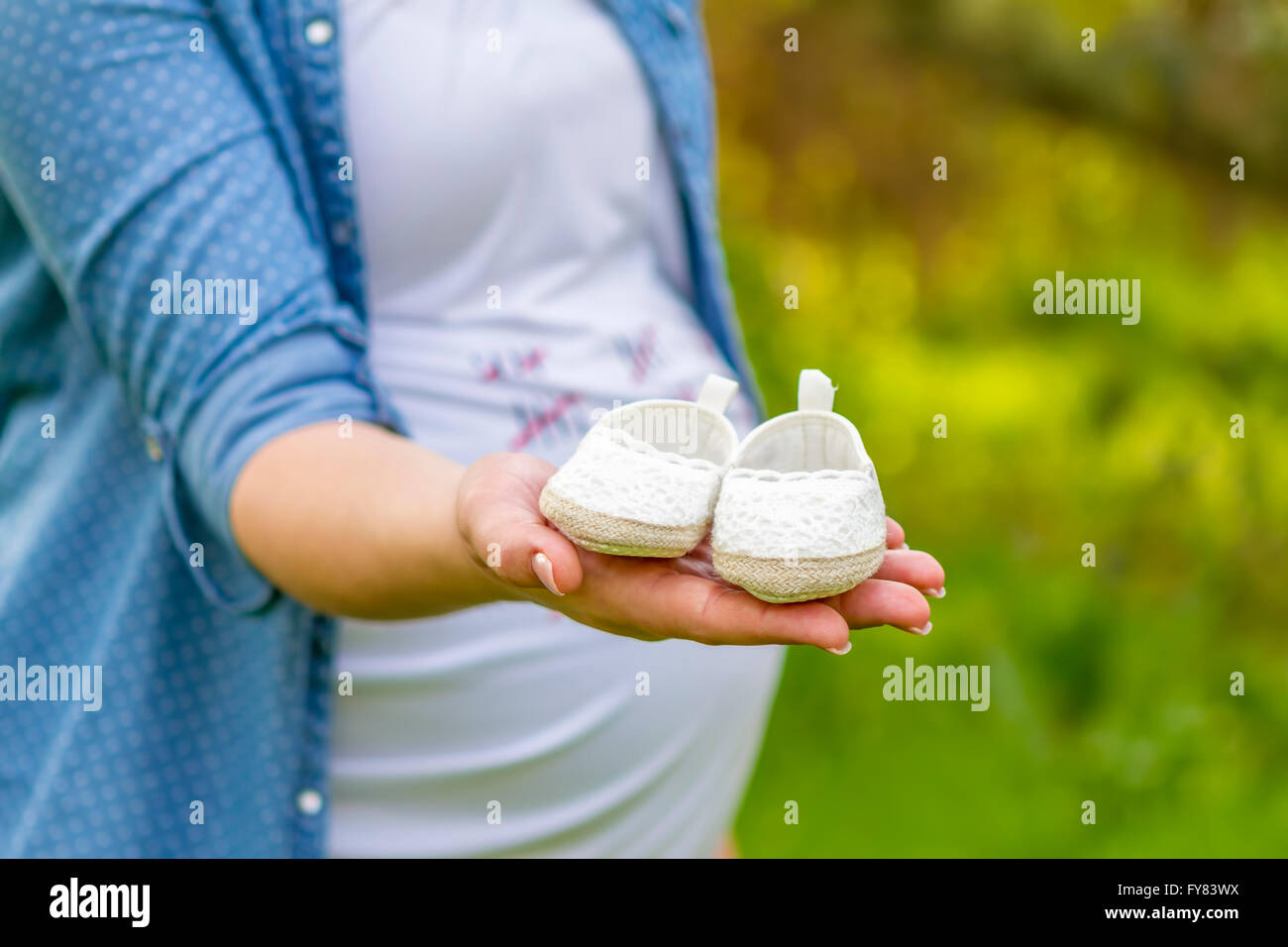 Close up of a pregnant woman holding baby shoes dans ses mains dans un parc. Banque D'Images