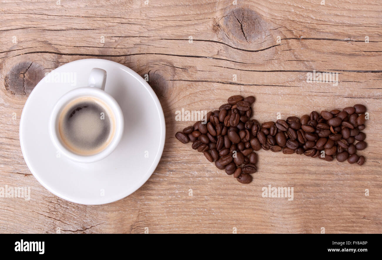 Les grains de café de flèche pointant sur une tasse de café, le tout sur une vieille planche de bois, disposition horizontale Banque D'Images