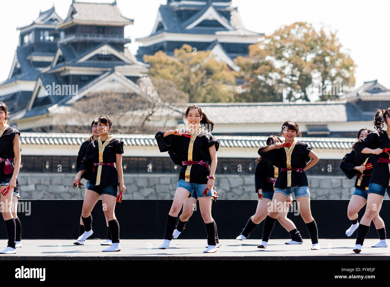 Japanese female dance troupe d'adolescentes, holding naruko, danser sur scène en plein air avec Château Kumamoto derrière eux, au cours de la fête de Yosakoi. Banque D'Images