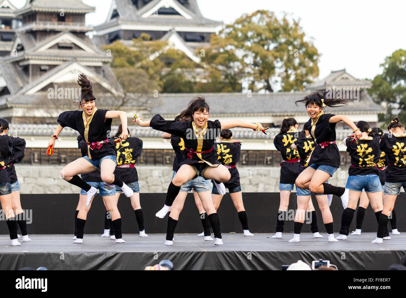 Japanese female dance troupe d'adolescentes, holding naruko, danser sur scène en plein air avec Château Kumamoto derrière eux, au cours de la fête de Yosakoi. Banque D'Images