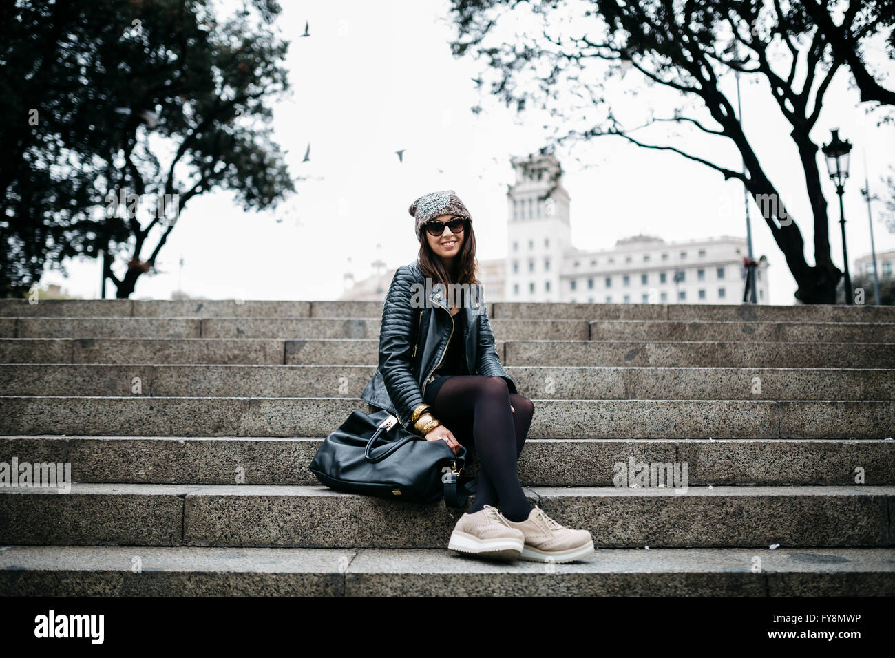 Espagne, Barcelone, smiling young woman sitting on stairs Banque D'Images