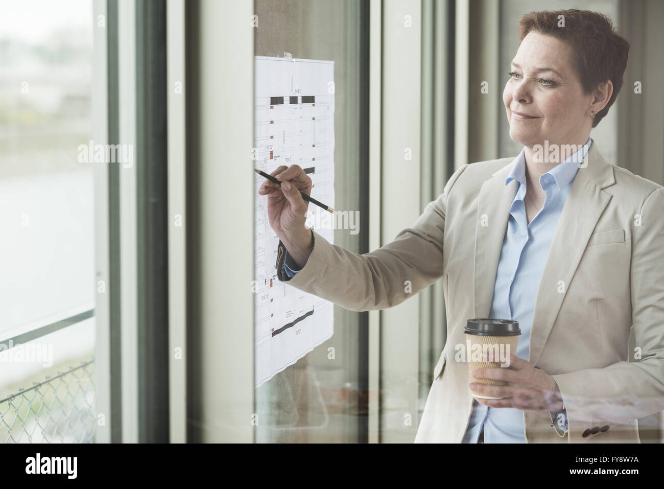 Confident businesswoman avec plan de construction à la fenêtre Banque D'Images
