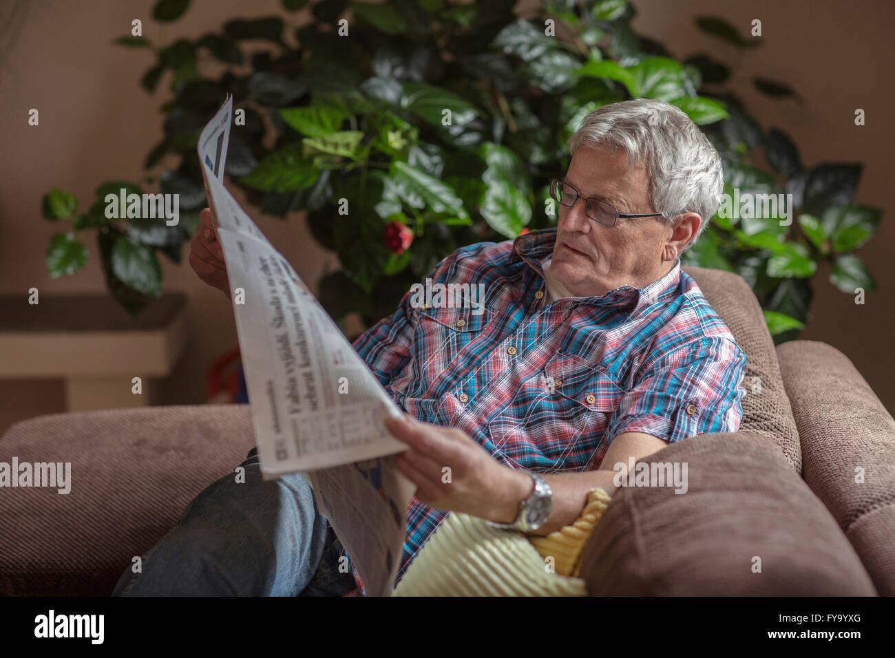 Homme, 64 ans, lire un journal sur le canapé Banque D'Images