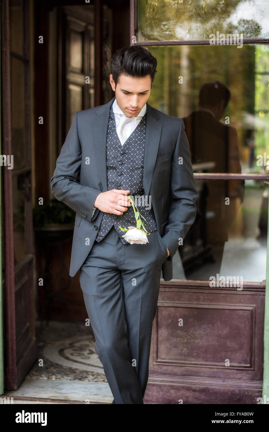 Portrait du jeune élégant costume gris en bridgegroom maintenant fleur blanche. Beau jeune homme en costume sombre attend sa femme Banque D'Images