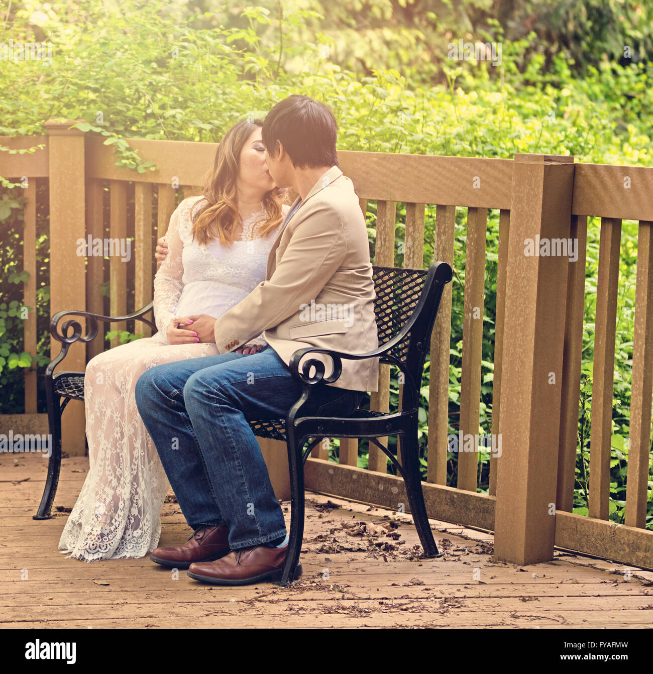 Attends maman et papa s'embrasser sur un banc de patio avec des bois en arrière-plan. Banque D'Images