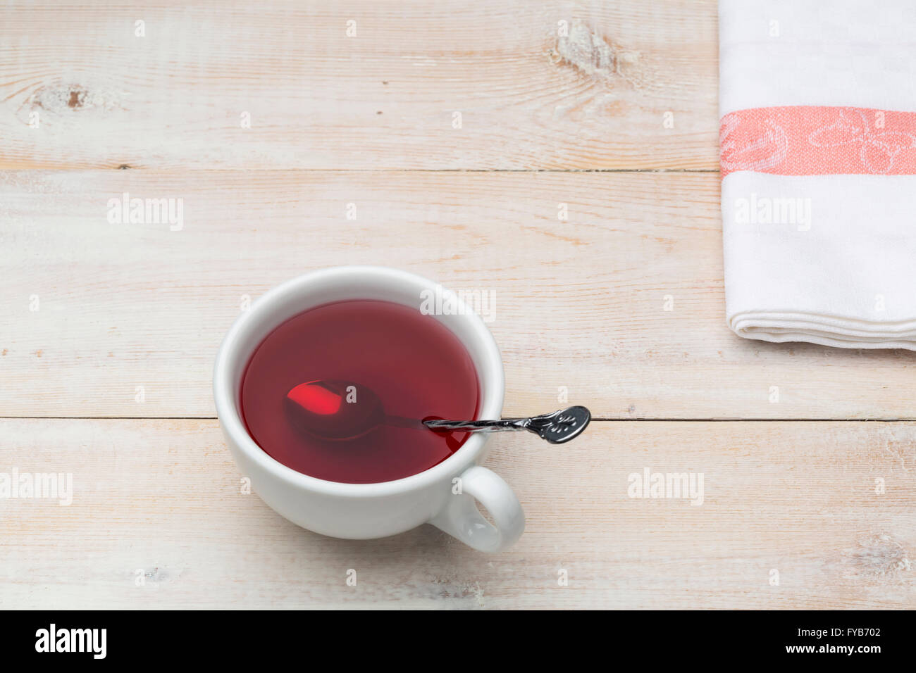 Tasse de thé rouge avec cuillère sur fond lumineux en bois Banque D'Images