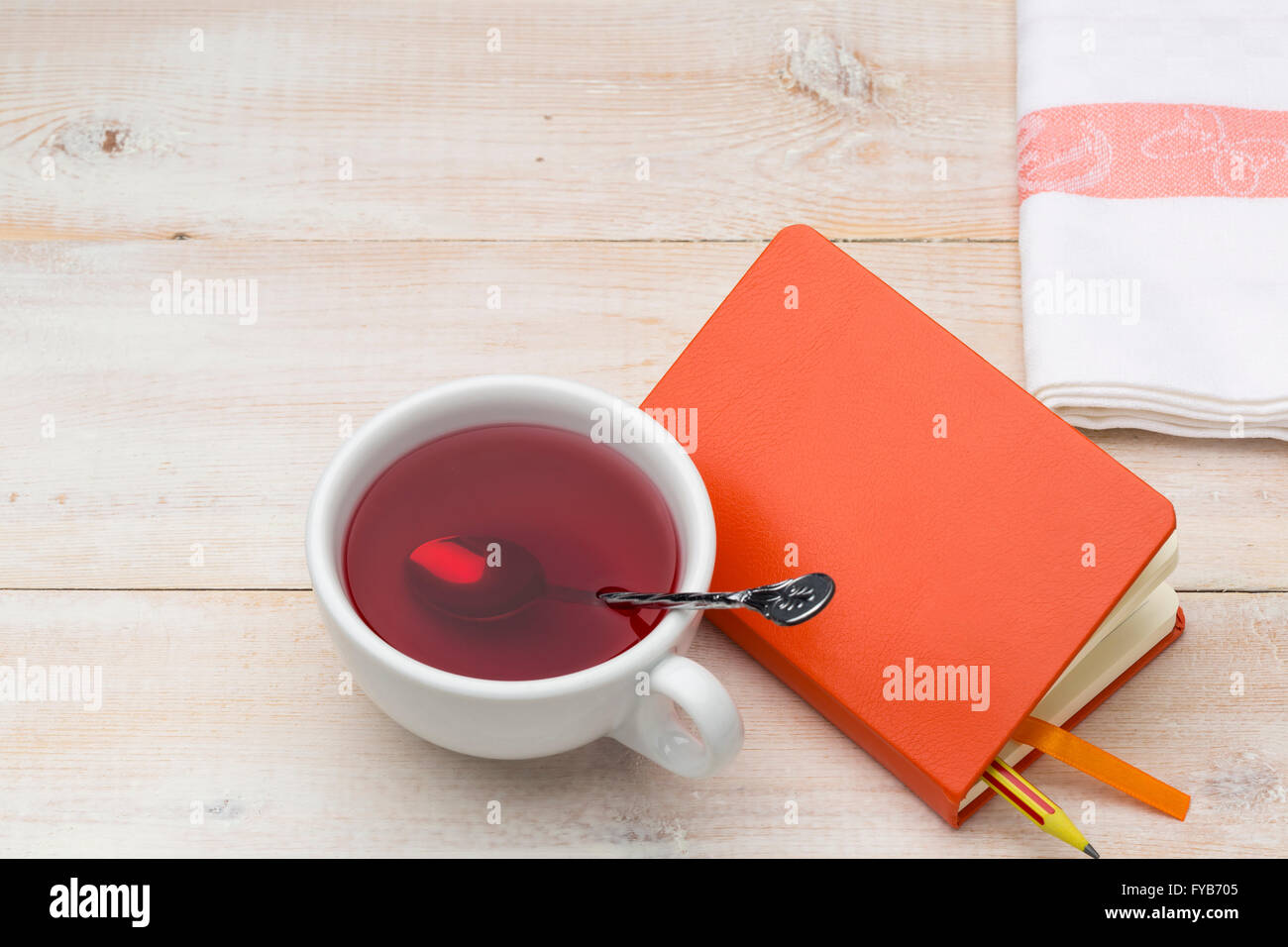 Tasse de thé rouge et orange sur le bloc-notes de fond en bois lumineux Banque D'Images