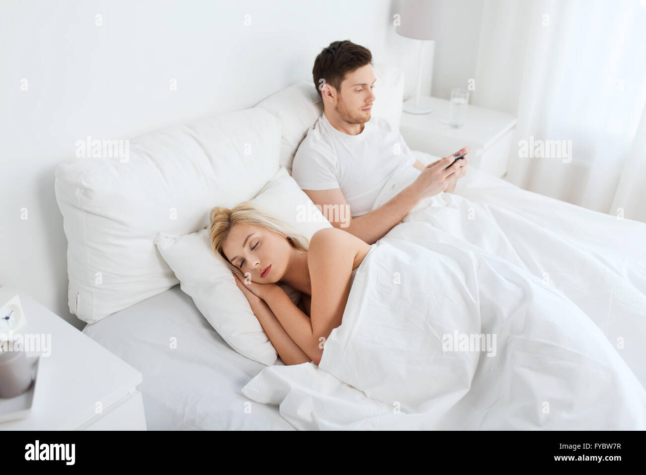 Man texting message tandis que la femme est sleeping in bed Banque D'Images
