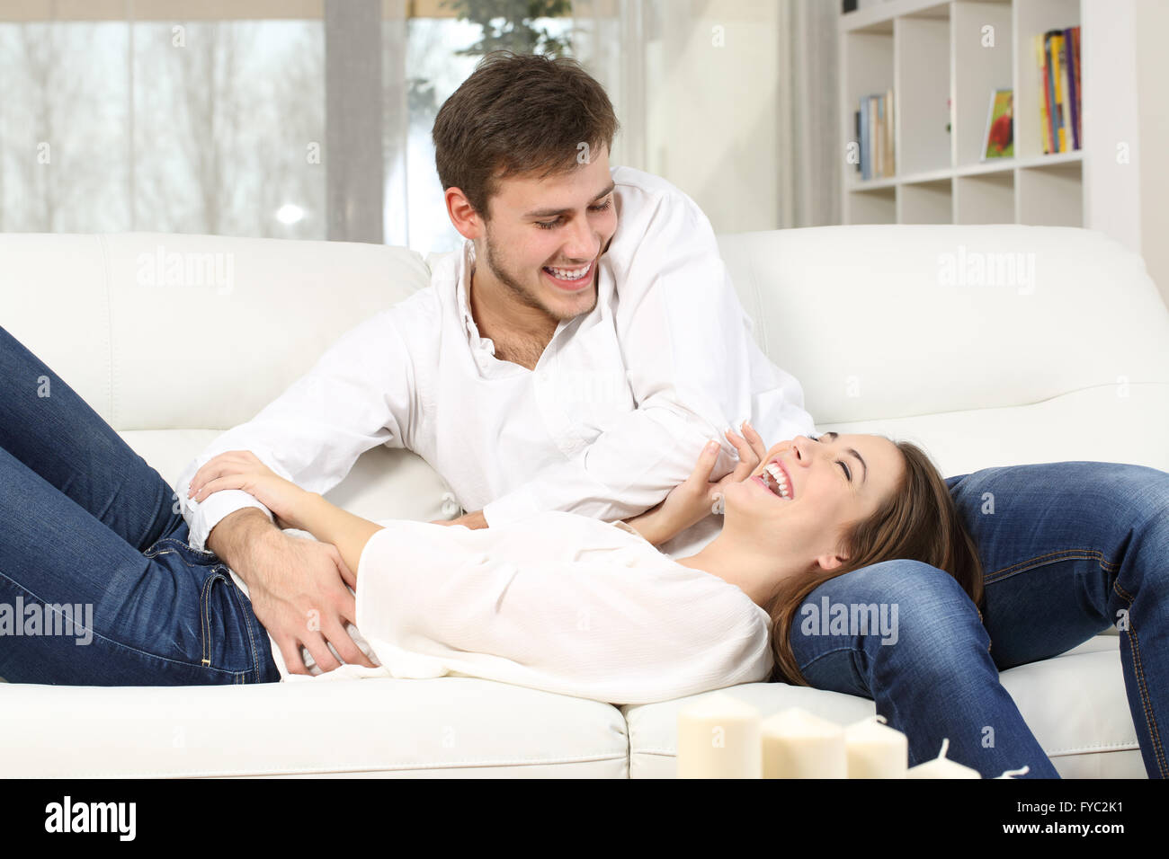 Playful couple ou mariage chatouillant et rire dans un canapé à la maison Banque D'Images