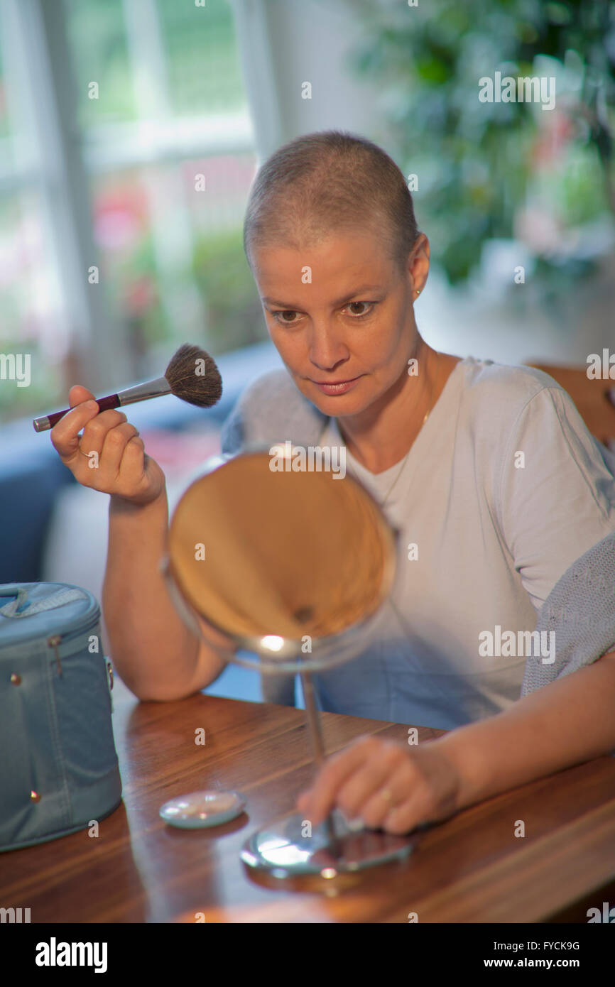 Femme, 48 ans, avec les cheveux courts après la chimiothérapie, appliquant le maquillage Banque D'Images