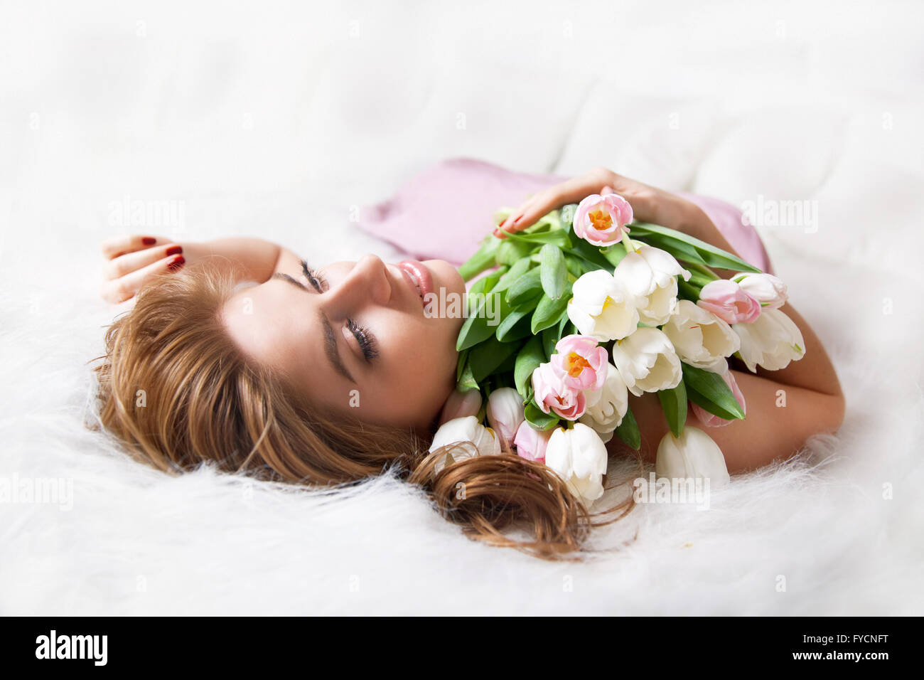 Jeune femme avec un bouquet de fleurs sur le lit. Banque D'Images