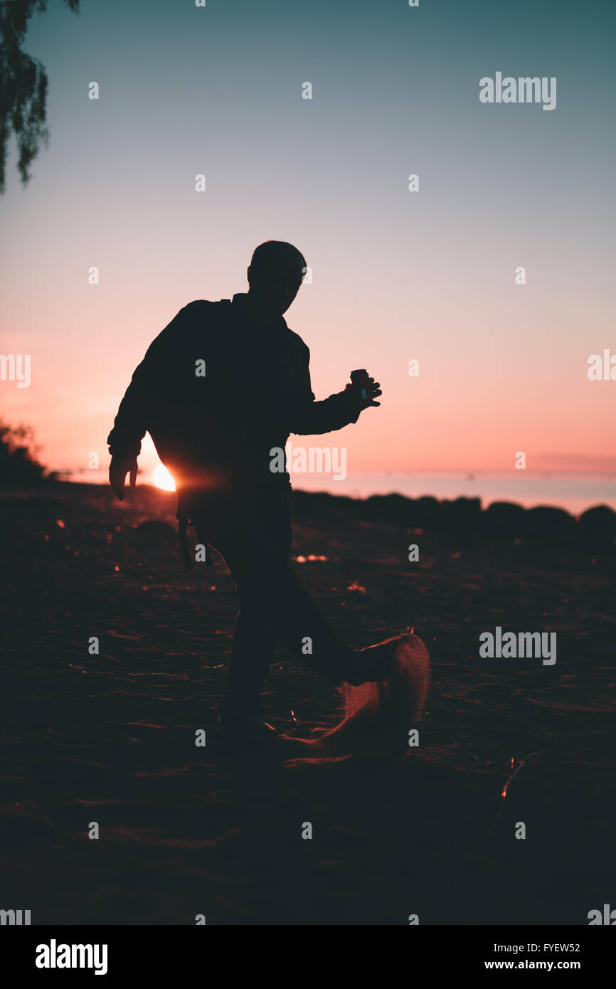 Silhouette de la personne tenant dans la main un verre dans une bouteille. Banque D'Images