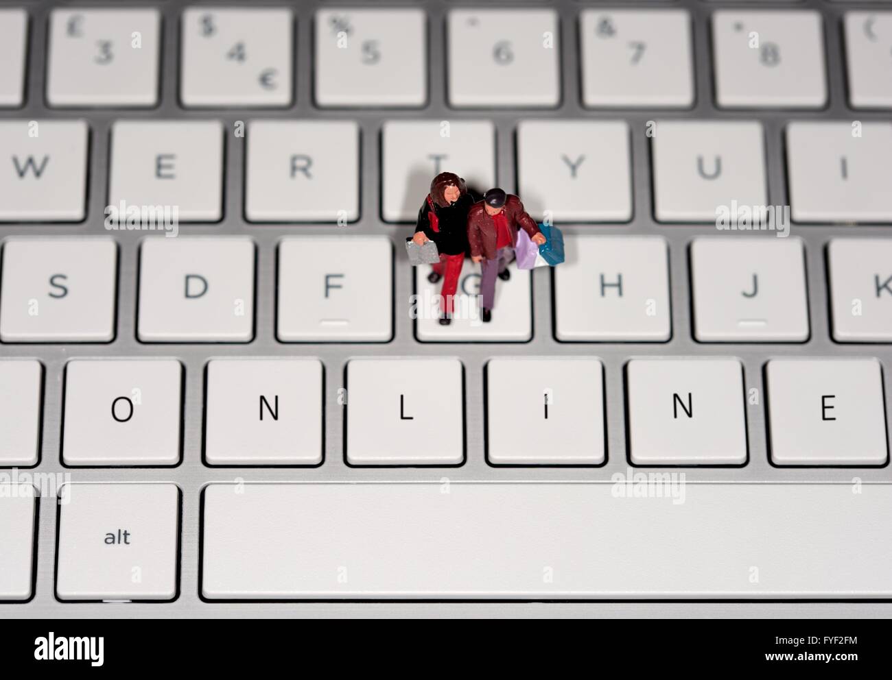 Une figurine miniature couple carrying shopping bags sur un clavier d'ordinateur portable avec le mot EN LIGNE édité numériquement sur les touches. Banque D'Images