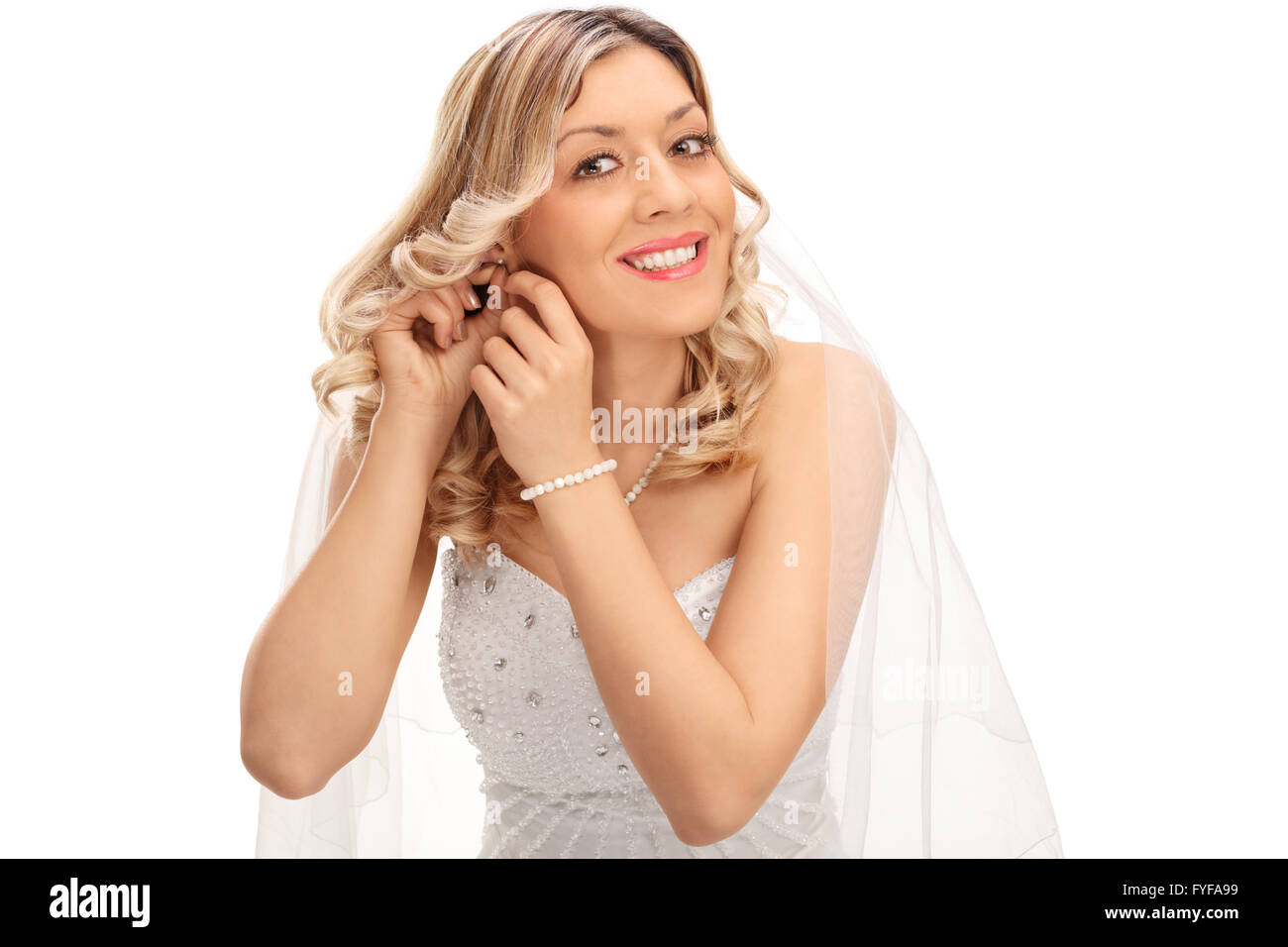 Jeune blonde bride mettre sur boucles d'oreilles et regardant la caméra isolé sur fond blanc Banque D'Images