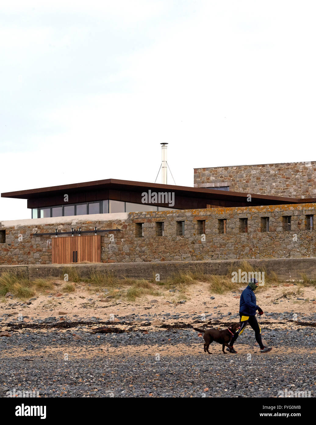 Voir à partir de la plage ci-dessous avec l'homme et le chien. Le Petit Fort, St Helier, Royaume-Uni. Architecte : architectes d'Hudson, 2016. Banque D'Images