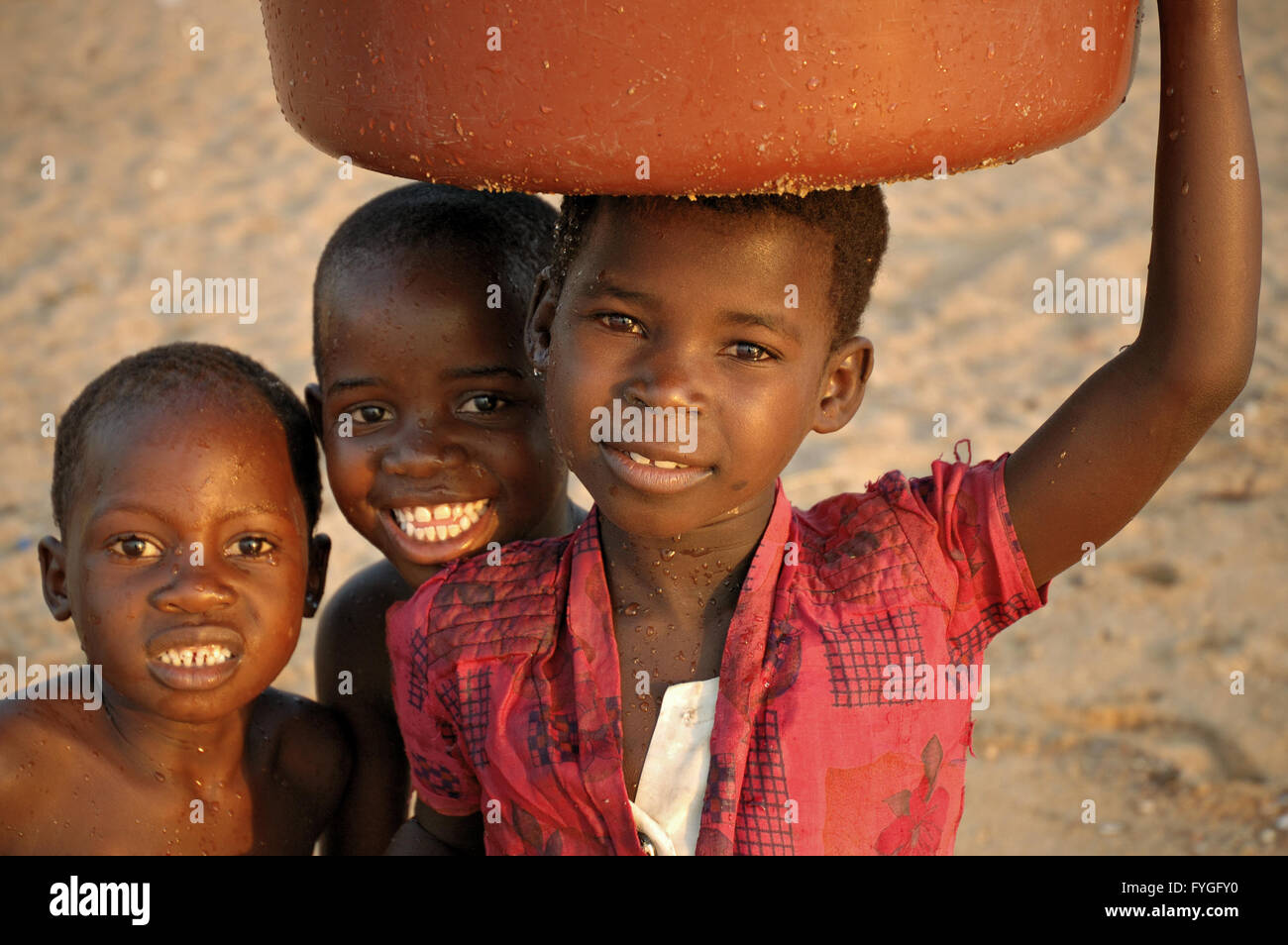 Groupe d'enfants avec une fille portant de l'eau sur sa tête sur la plage de Cape Maclear, Malawi Banque D'Images