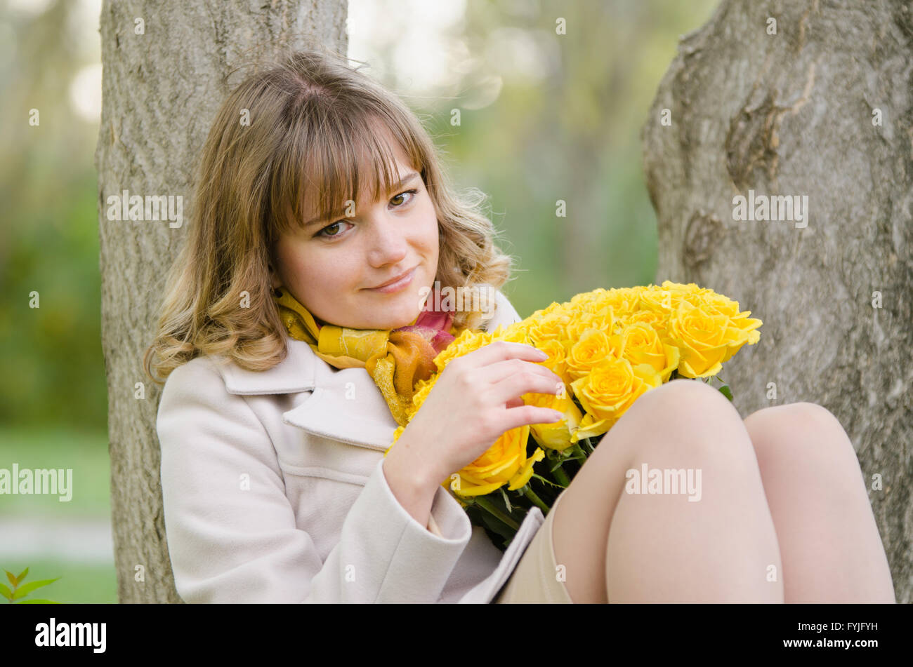 Triste fille avec des roses jaunes, assis dans un arbre Banque D'Images