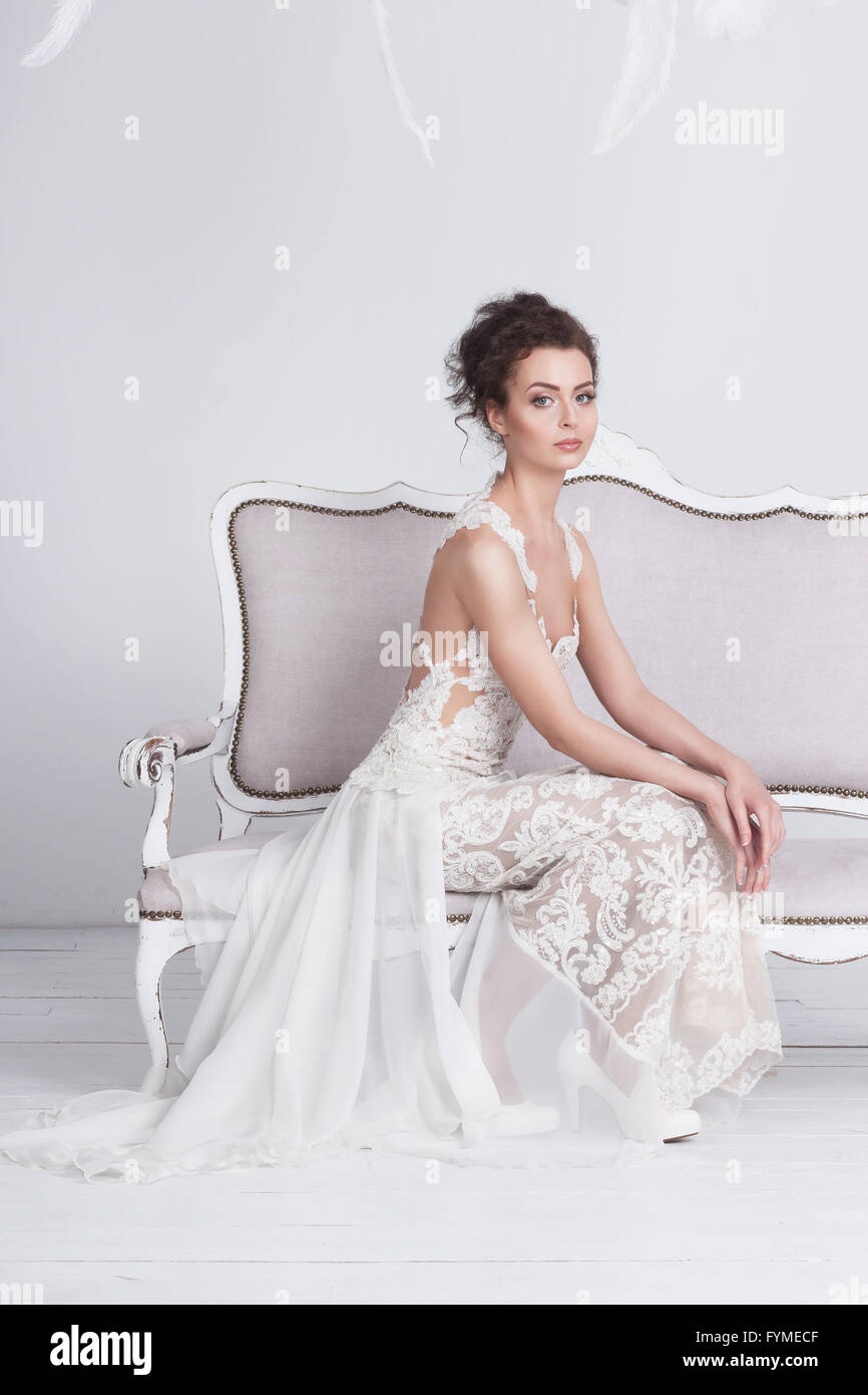 Belle jeune femme dans une luxueuse dentelle robe de mariage. Elle siège sur un canapé vintage blanc. Elle est un élégant et mince, elle a t Banque D'Images