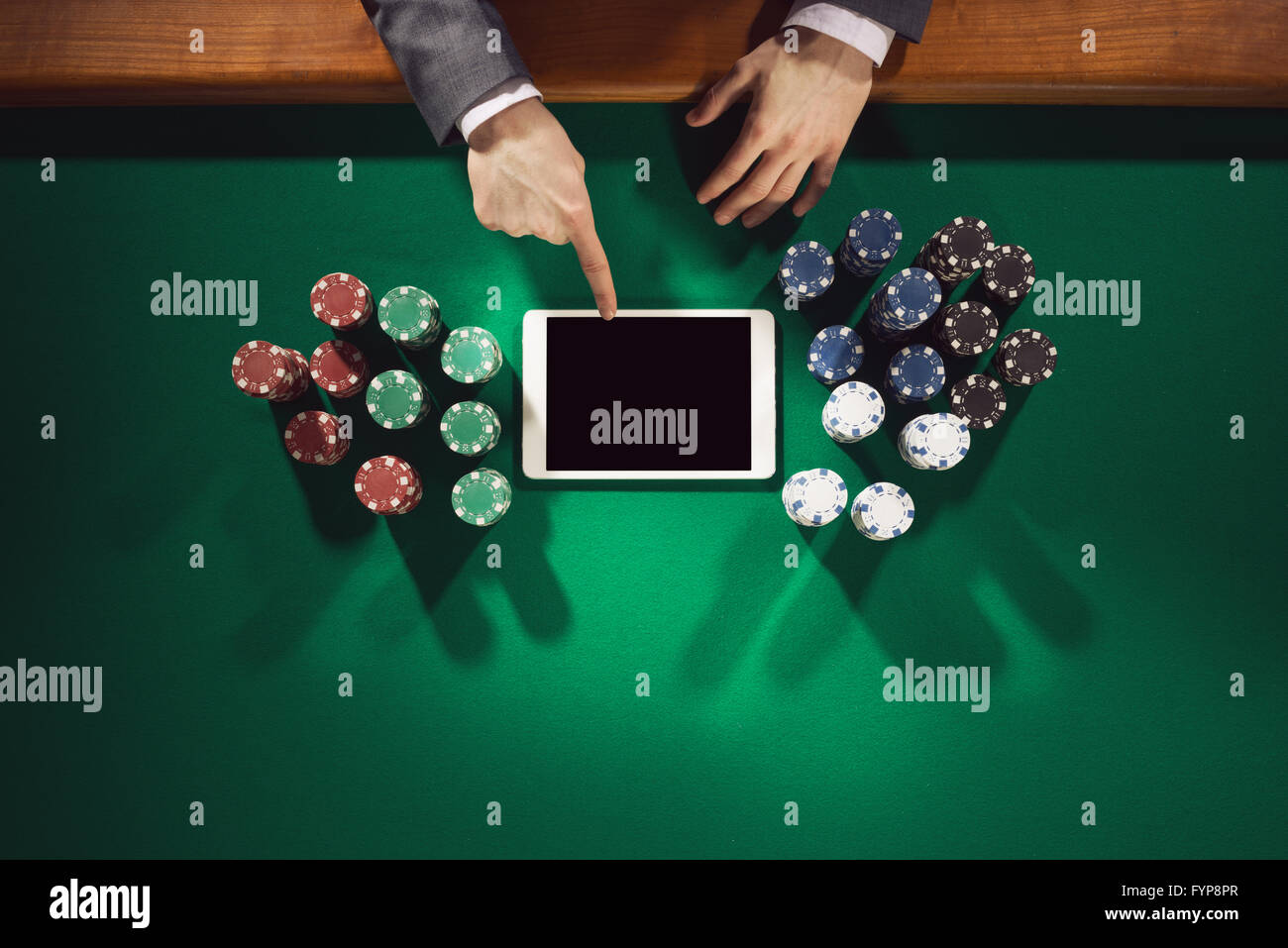 Joueur élégant mâle touchant une tablette numérique avec écran tout autour de jetons sur la table verte, vue du dessus Banque D'Images