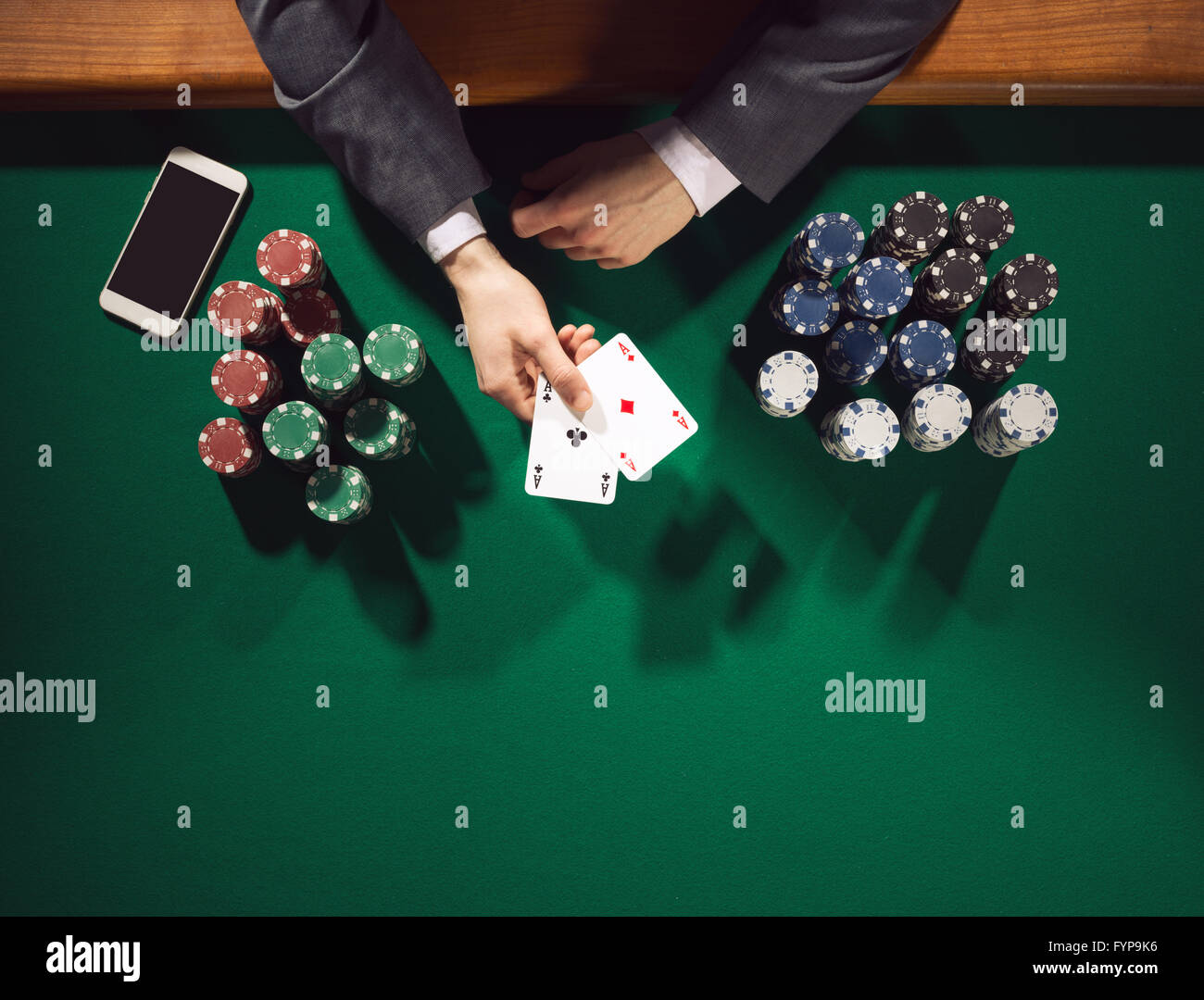 Joueur de poker homme élégant avec deux as holding smartphone avec des piles de jetons tout autour, les mains détail Vue de dessus Banque D'Images