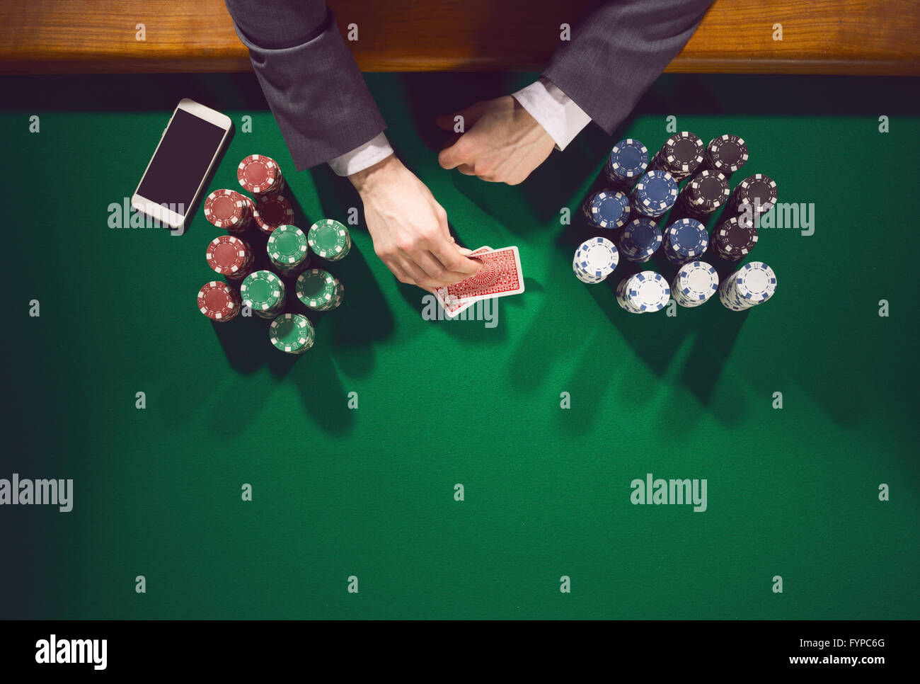 Homme élégant smartphone avec joueur de poker à la recherche de ses cartes avec des piles de jetons tout autour de Banque D'Images