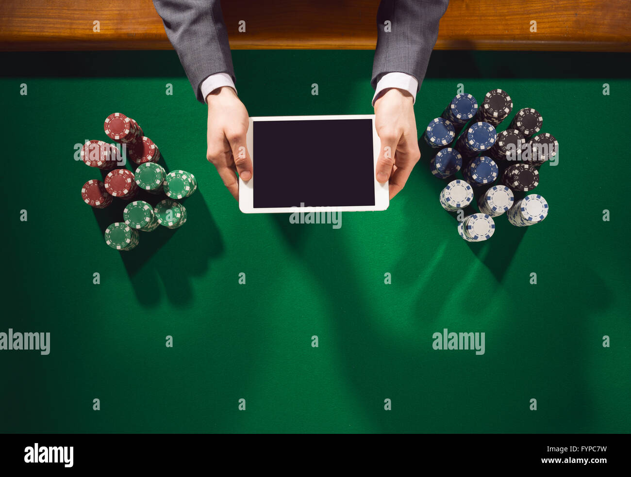 Lecteur mâle tenant une tablette numérique et jouer avec des piles de jetons tout autour sur un tableau vert, vue du dessus Banque D'Images