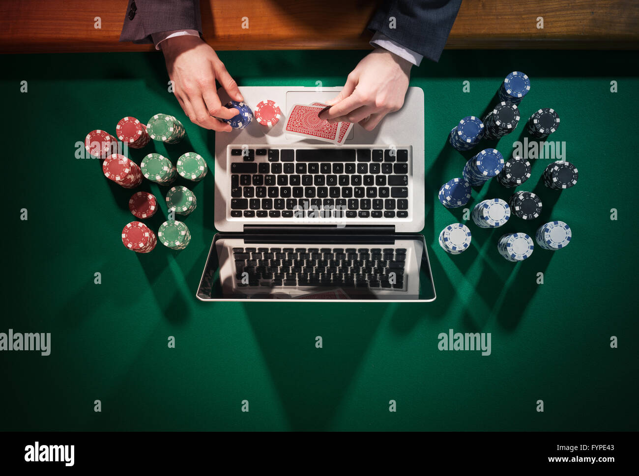 Homme jouant au poker en ligne avec un ordinateur portable sur une table avec tous les jetons verts autour de vue de dessus, il est en train de regarder ses cartes Banque D'Images