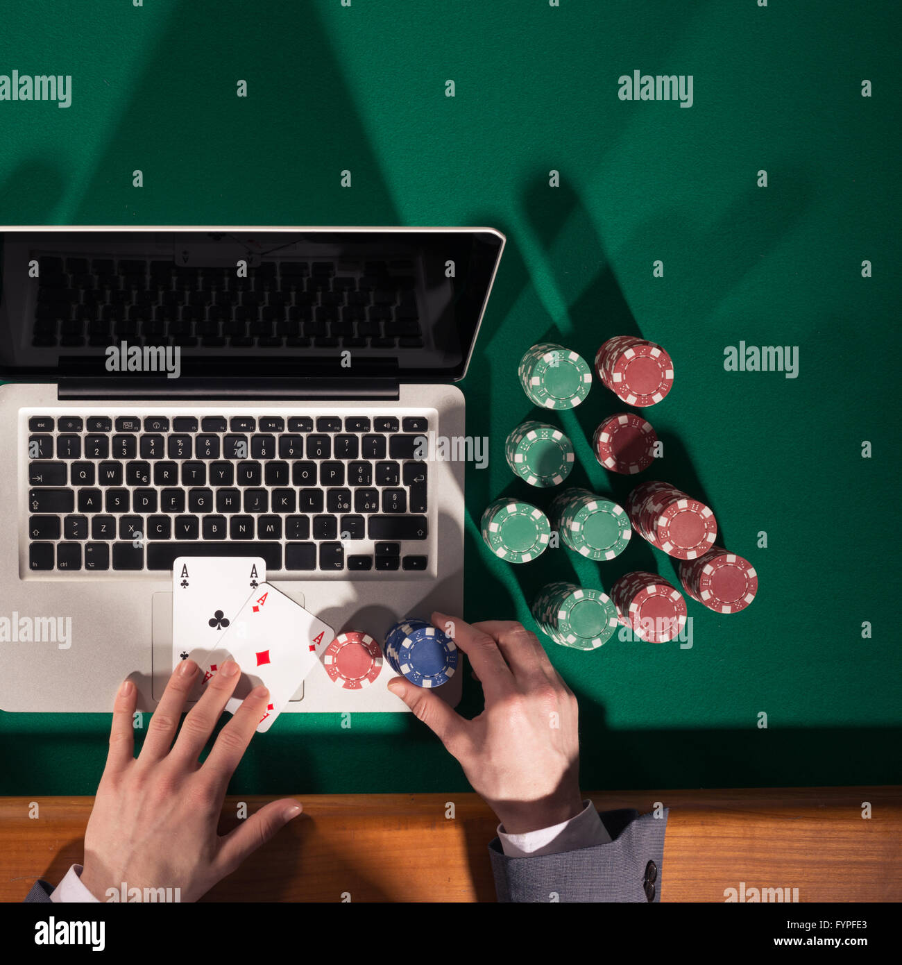 Homme jouant au poker en ligne avec un ordinateur portable sur une table avec tous les jetons verts autour, vue du dessus Banque D'Images