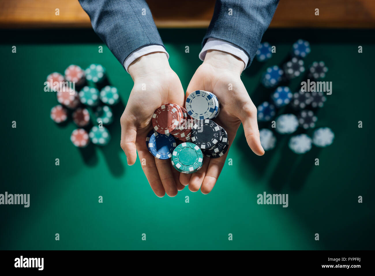 Homme élégant casino joueur tenant une poignée de jetons en arrière-plan sur la table verte, mains close up Vue de dessus Banque D'Images