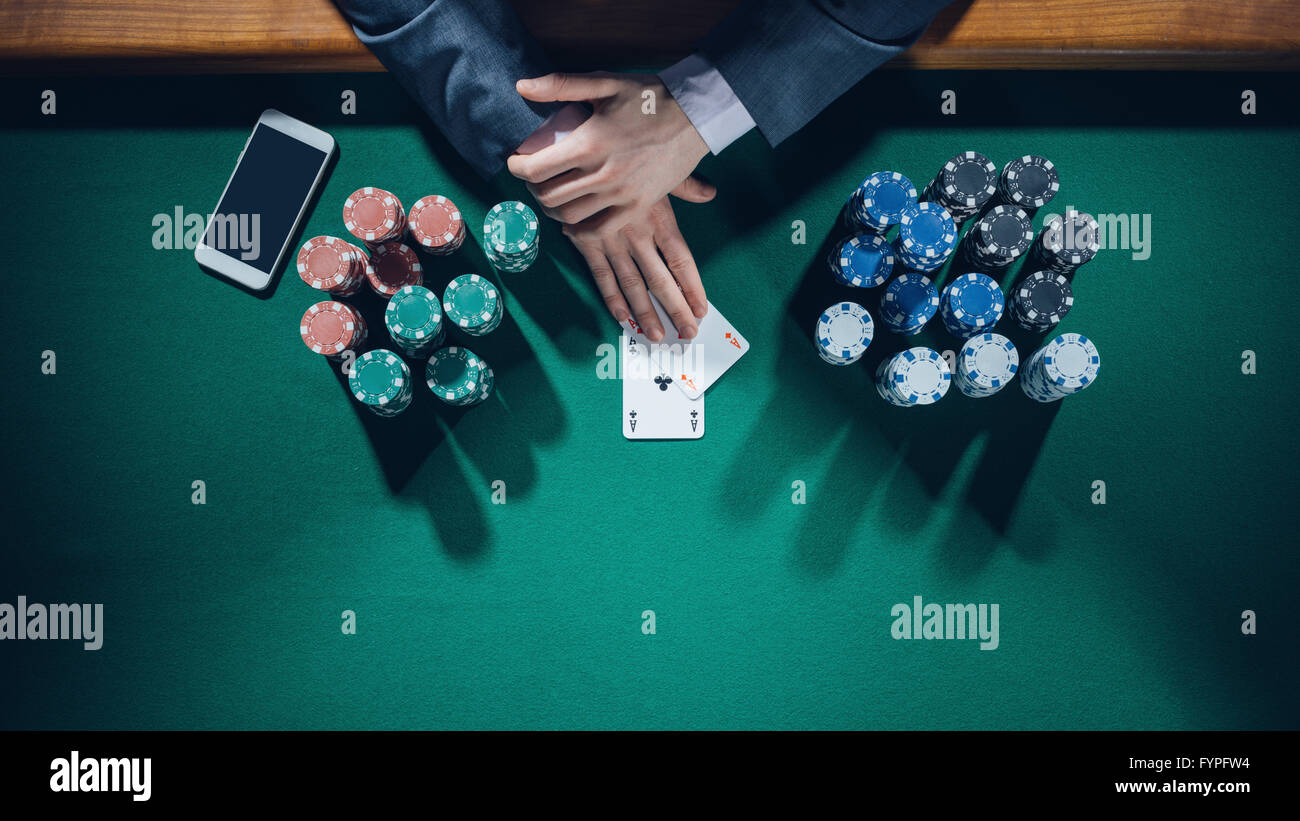Joueur de poker homme élégant avec deux as holding smartphone avec des piles de jetons tout autour, les mains détail Vue de dessus Banque D'Images
