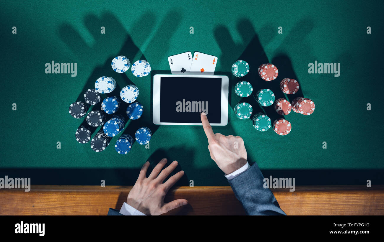 Poker player's hands with digital tablet, piles de jetons et cartes sur table verte, vue du dessus Banque D'Images