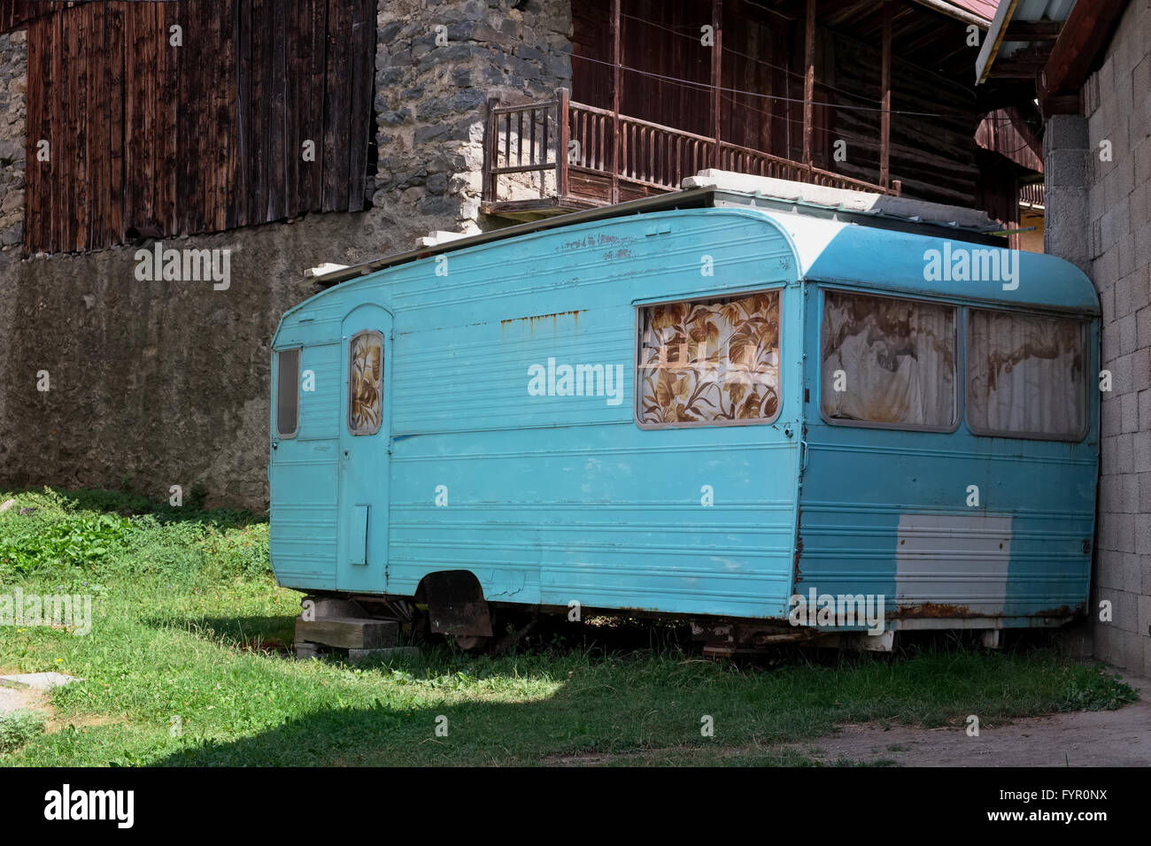 Old rusty jacked up trailer home debout sur un champ entre les anciennes maisons faites de blocs. Banque D'Images