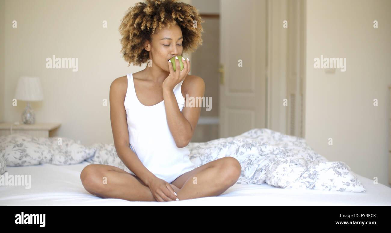 Woman Sitting on Bed And Eating Apple Banque D'Images