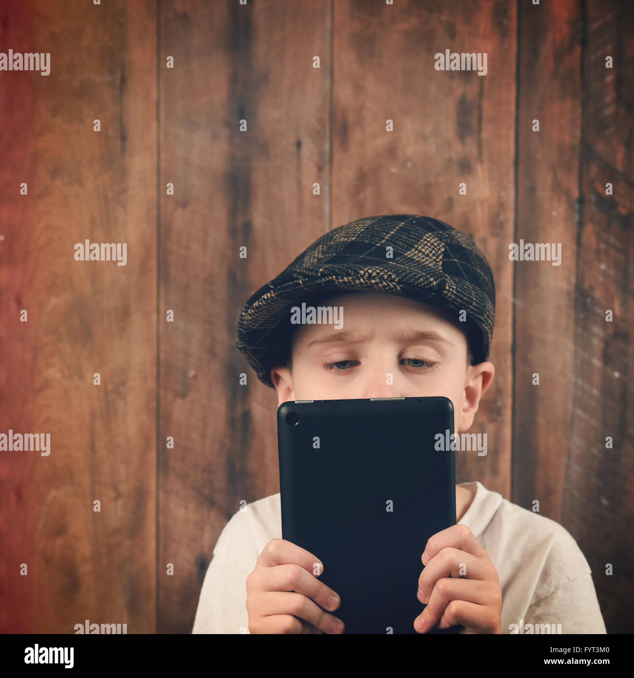 Un garçon est maintenant une technologie Tablet et lecture d'un écran. L'enfant a un vintage hat avec un bois bg pour la communication idée. Banque D'Images