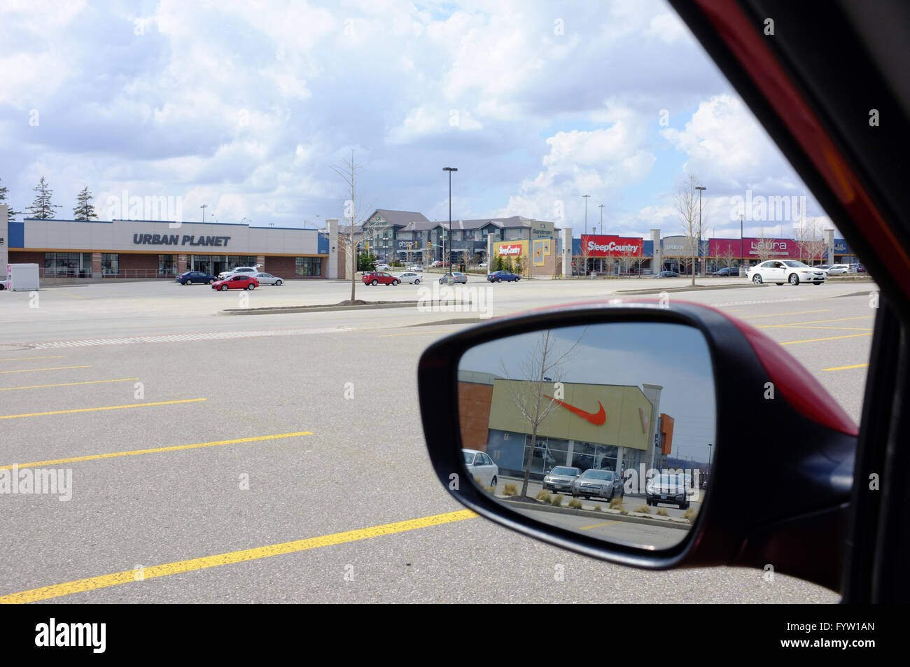Le logo de Nike se reflète dans le miroir de l'aile d'une voiture garée dans un grand centre commercial parking. Banque D'Images