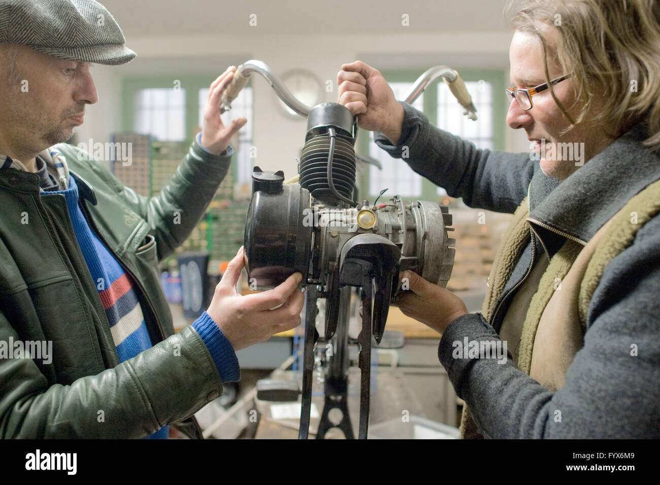 Berlin, Allemagne. 22 avr, 2016. Frank David (L) par les pairs et Kahn, employés de Velo Solextours, placer un cylindre d'un moteur à deux temps sur le châssis à l'aide du cric d'un cyclomoteur Solex dans l'atelier de l'entreprise à Berlin, Allemagne, 22 avril 2016. Le Velosolex, l'équivalent français d'un cyclomoteur, célèbre son 70e anniversaire. Les amateurs peuvent prendre les véhicules sur un tour d'essai à Berlin. Photo : KLAUS-DIETMAR GABBERT/dpa/Alamy Live News Banque D'Images