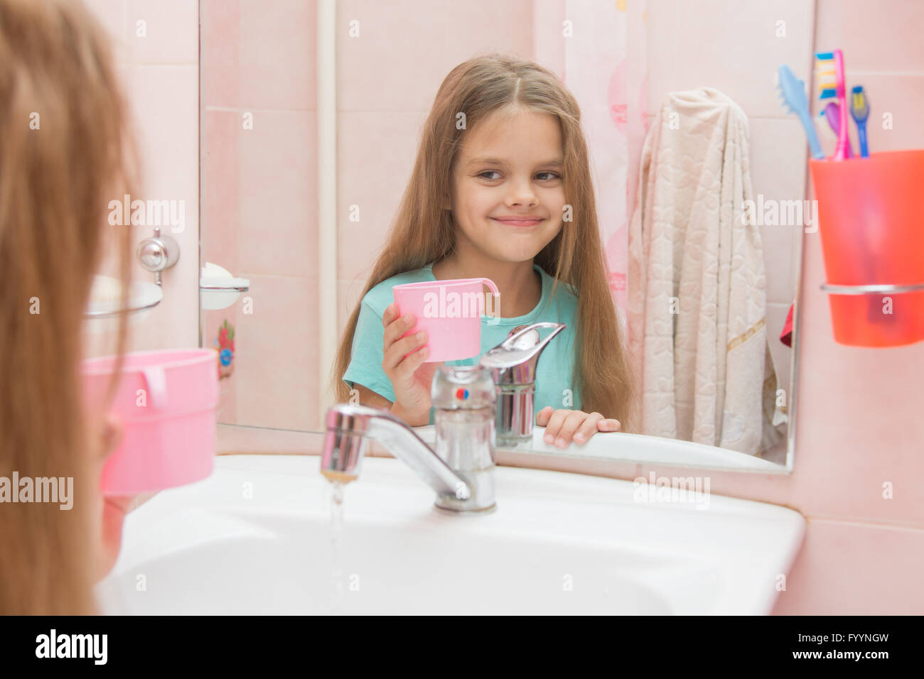 Happy girl holding a cup et regarde dans le miroir dans la salle de bains Banque D'Images