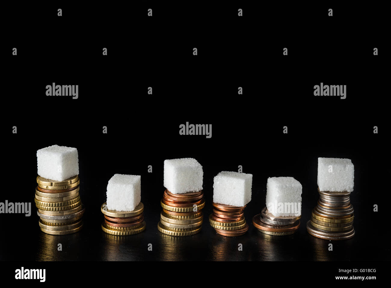 Des piles de pièces de monnaie avec des morceaux de sucre et des bouteilles remplies de sucre sur le dessus, symbolisant l'impôt sur le sucre, sur fond d'ardoise noire Banque D'Images