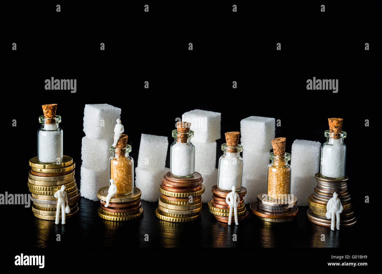 Des piles de pièces de monnaie avec des morceaux de sucre et des bouteilles remplies de sucre sur le dessus, symbolisant l'impôt sur le sucre, sur fond d'ardoise noire Banque D'Images