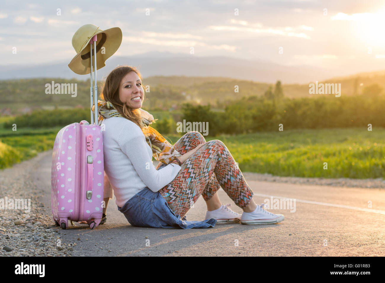 Lonely Girl assis sur la route près de sa valise Banque D'Images