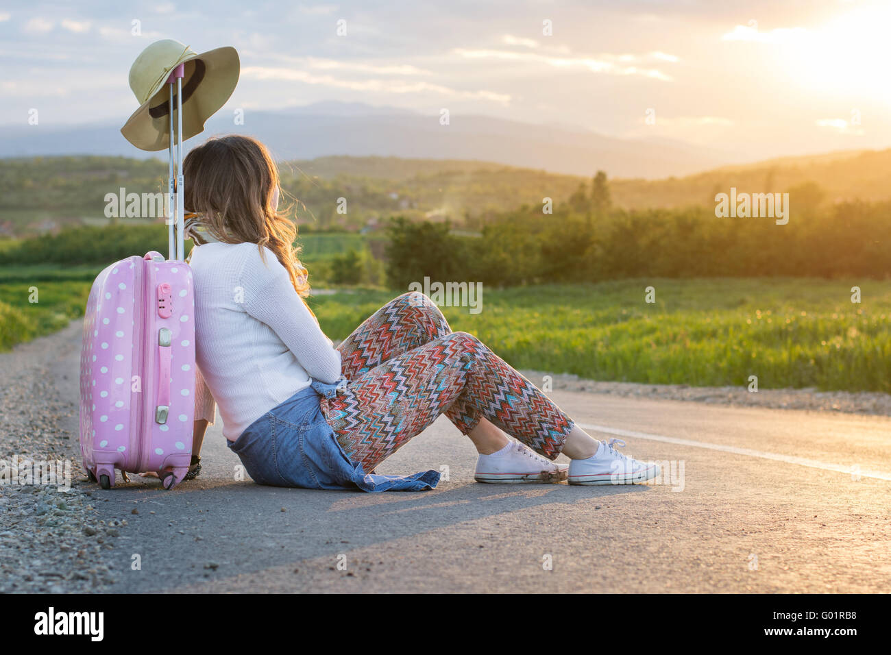 Lonely Girl assis sur la route près de sa valise Banque D'Images