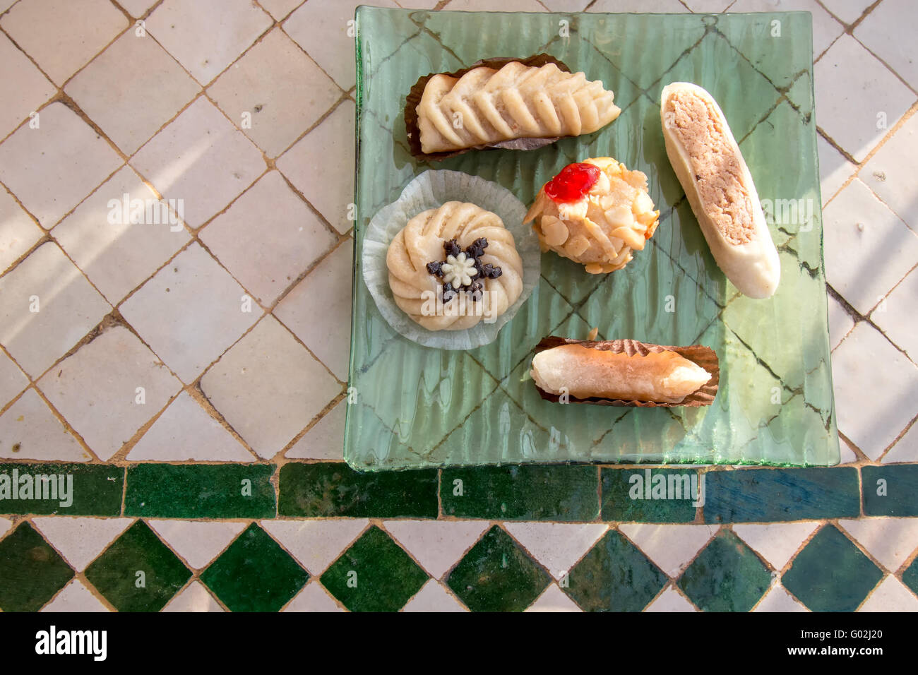 Comme de petits bijoux, assortiment de bonbons traditionnels arabes, servis sur une plaque verte et table en mosaïque. Banque D'Images