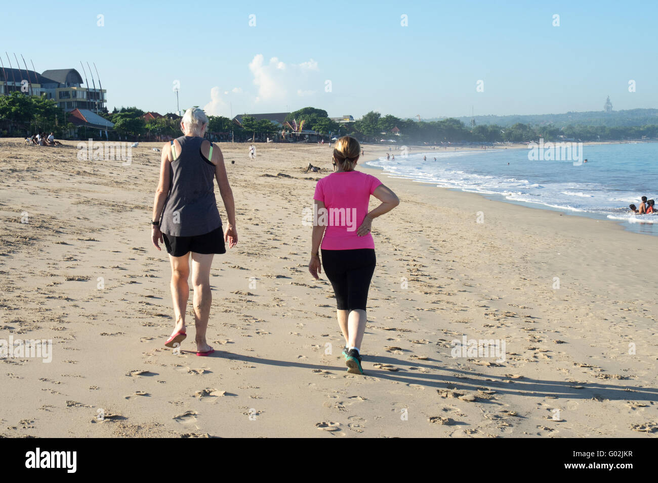 Deux femmes marchant le long de la plage de La Baie de Jimbaran, Bali. Banque D'Images