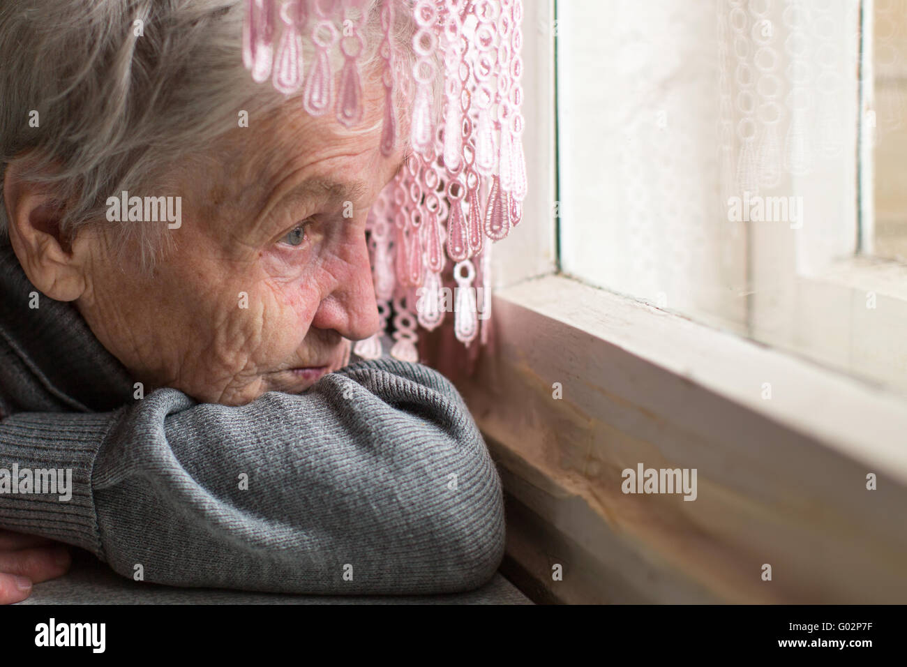 Une femme âgée a tristement par la fenêtre, face close-up. Banque D'Images