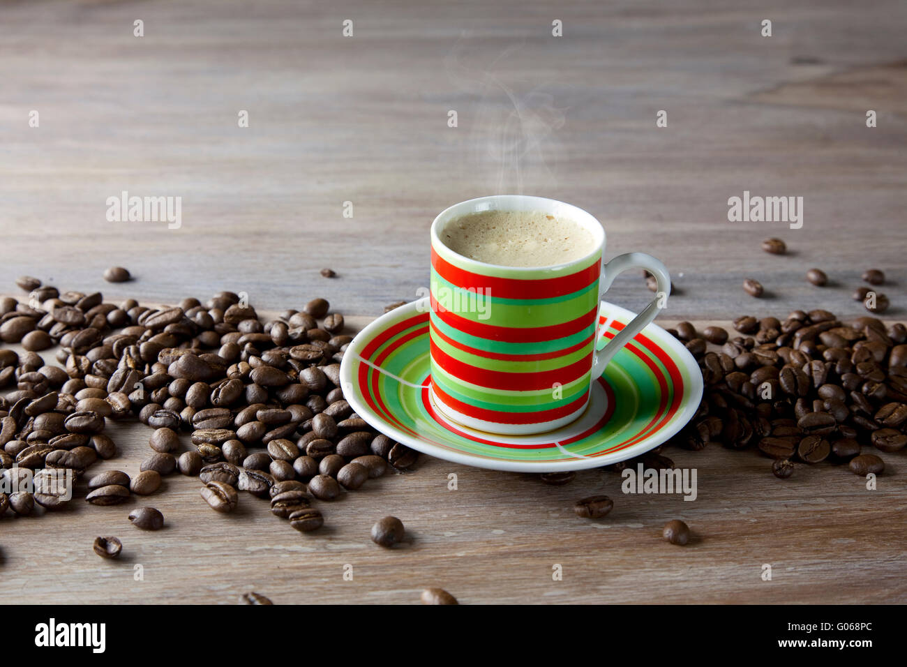 Café chaud dans la tasse à rayures avec des haricots sur la table en bois Banque D'Images